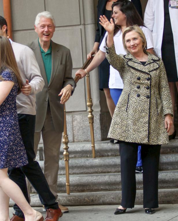 Hillary Clinton und Bill Clinton stehen lächelnd auf einer Treppe und winken.