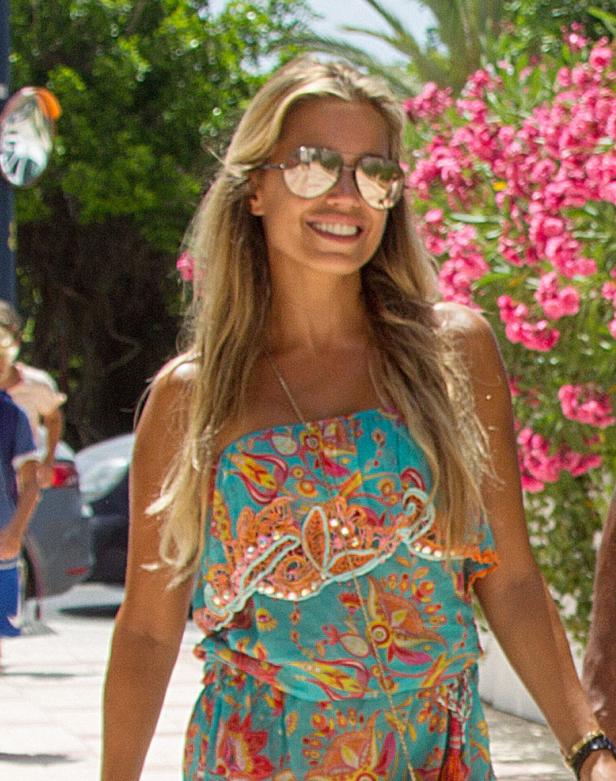Eine Frau mit Sonnenbrille und einem bunten Sommerkleid lächelt.
