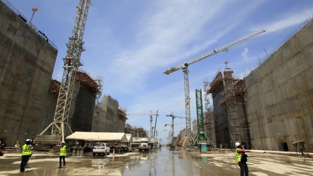 Mehrere Baukräne ragen zwischen hohen Betonwänden auf einer Baustelle in den Himmel.