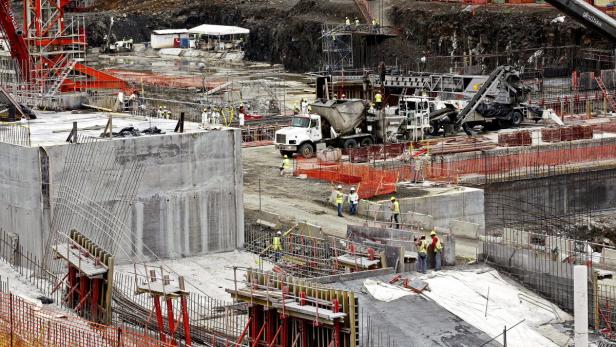 Auf einer Baustelle arbeiten Bauarbeiter an Betonstrukturen und mit einem Betonmischer.