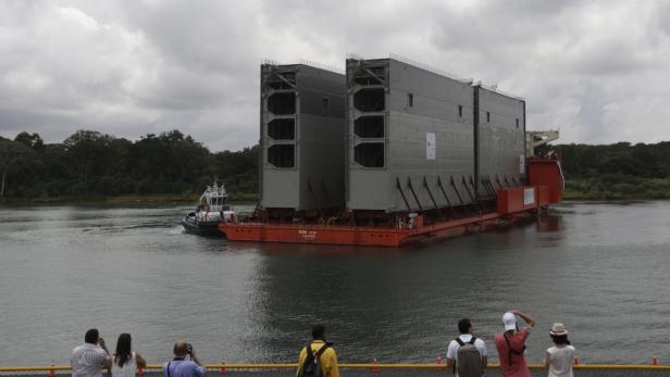 Ein Schlepper zieht eine Barge mit zwei großen Schleusentoren durch einen Kanal.