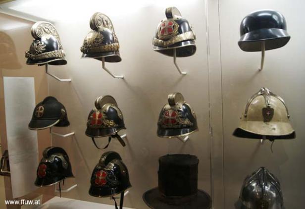 Eine Sammlung historischer Helme und Hüte in einer Vitrine.