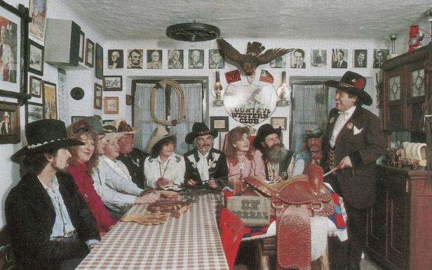 Eine Gruppe von Personen in Cowboy-Kleidung sitzt an einem Tisch in einem dekorierten Raum.