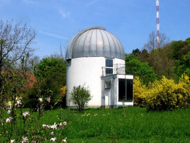 Ein kleines Observatorium mit einer silbernen Kuppel inmitten einer grünen Landschaft.