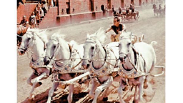 Ein Mann fährt ein von vier weißen Pferden gezogenes Streitwagenrennen.