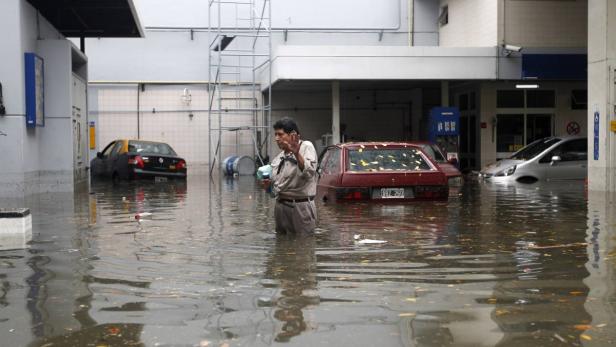 Ein Mann watet durch eine überflutete Straße, auf der mehrere Autos im Wasser stehen.