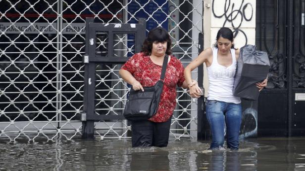 Zwei Frauen waten durch das knietiefe Wasser vor einem Geschäft.