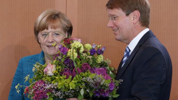Angela Merkel hält einen Blumenstrauß von einem Mann im Anzug entgegen.