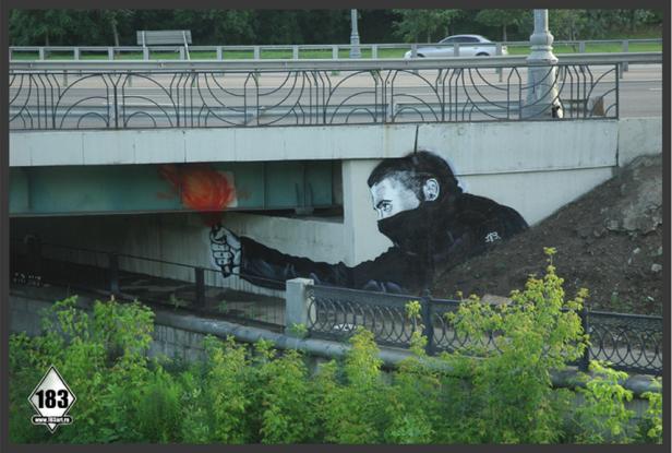 Ein Graffito unter einer Brücke zeigt eine vermummte Person mit einer Fackel.