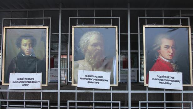 Drei Porträts von Puschkin, Sokrates und Mozart hängen an einem Gitter.