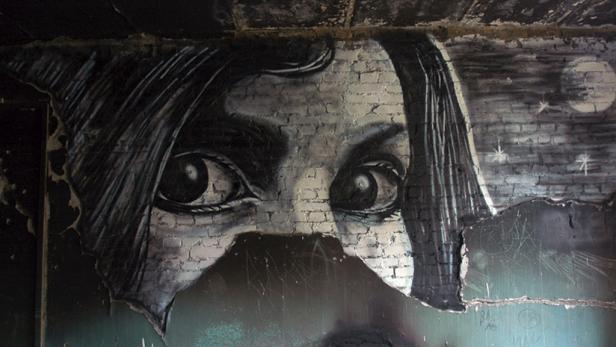 Ein Graffito an einer Ziegelwand zeigt das Gesicht einer Frau mit großen Augen vor einem Nachthimmel.