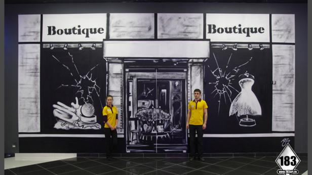 Zwei Personen stehen vor einer gemalten Boutique-Fassade.