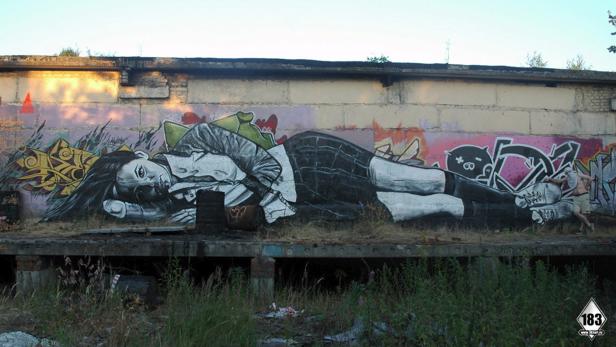 Ein Graffiti zeigt eine liegende Frau auf einer Mauer.