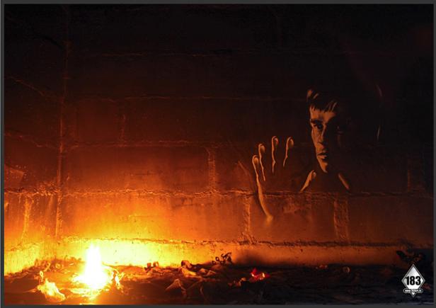 Ein Mann steht in einem dunklen Raum mit einem Feuer im Vordergrund.