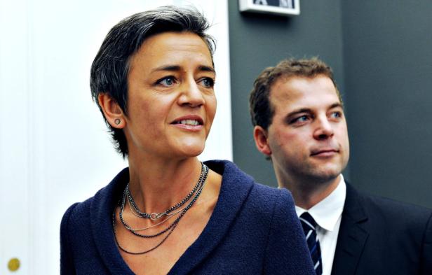 Eine Frau mit kurzem, dunklem Haar und ein Mann im Anzug schauen zur Seite.