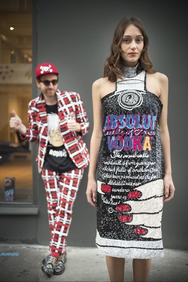 Eine Frau in einem Paillettenkleid mit „Absolut Vodka“-Aufschrift, daneben ein Mann im karierten Anzug.