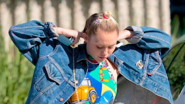 Eine junge Frau mit bunten Haarspangen richtet ihre Jeansjacke.