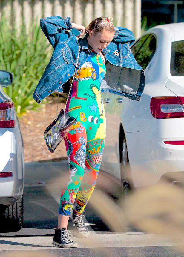 Eine Frau mit Jeansjacke und buntem Overall steht auf der Straße.