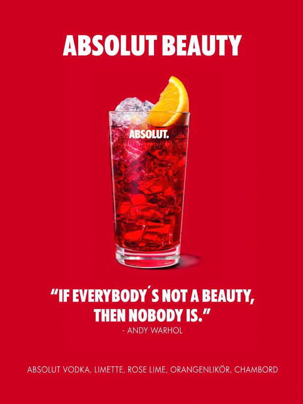 Ein Glas mit einem roten Cocktail, Eis und einer Orangenscheibe vor rotem Hintergrund.