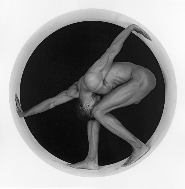 Ein Mann posiert nackt in einer kreisförmigen Öffnung.