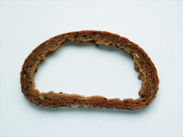 Ein leergegessenes Stück Roggenbrot mit Sonnenblumenkernen liegt auf einem weißen Untergrund.