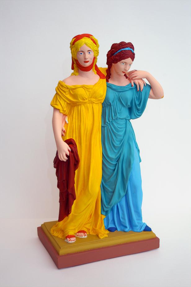 Eine bemalte Statue zweier Frauen in farbenfrohen Gewändern, die sich umarmen.