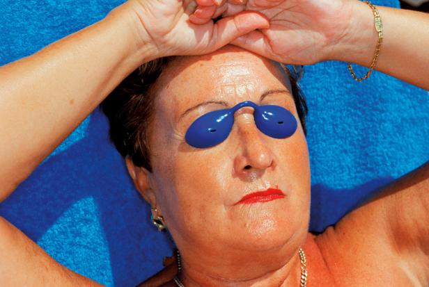 Eine Frau liegt mit blauen Augenschutz auf einem blauen Handtuch in der Sonne.