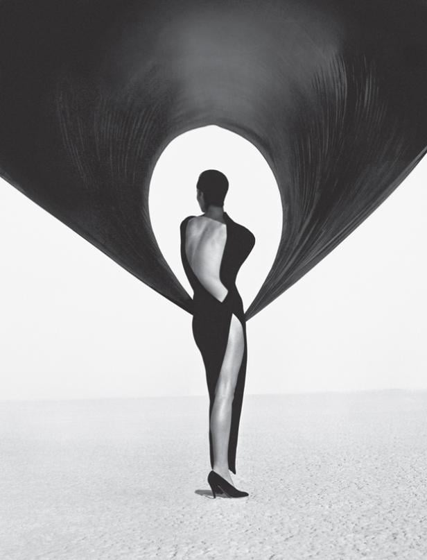 Eine Frau in einem schwarzen Kleid mit hohem Schlitz steht unter einem drapierten Stoff.