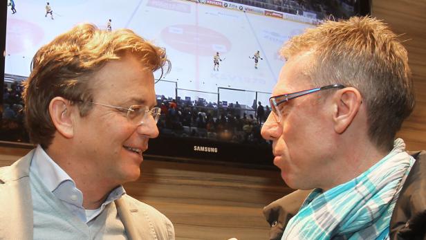 Zwei Männer unterhalten sich vor einem Fernseher, auf dem ein Eishockeyspiel läuft.
