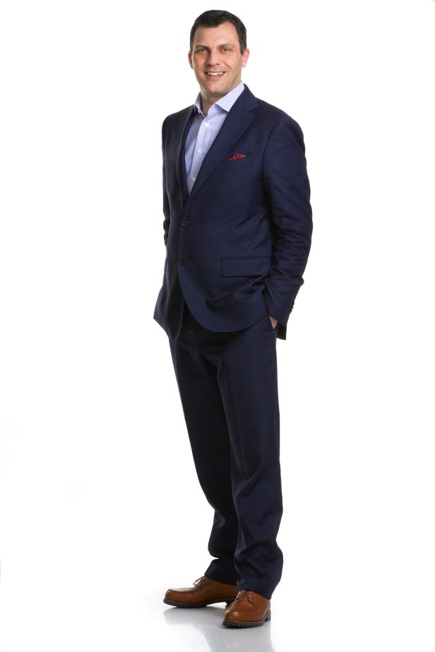 Ein Mann in einem blauen Anzug steht mit den Händen in den Hosentaschen.