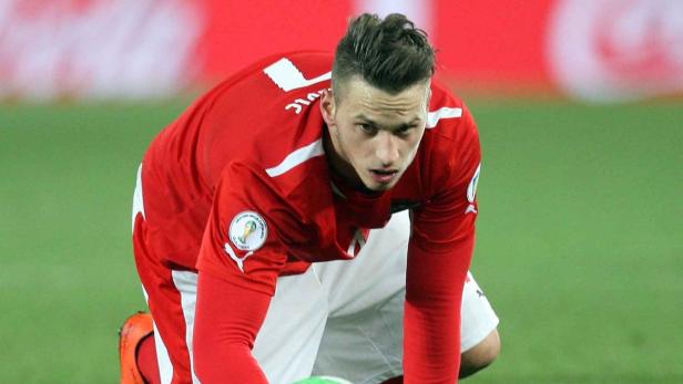 Ein Fußballspieler in roter Spielkleidung kniet auf dem Rasen.