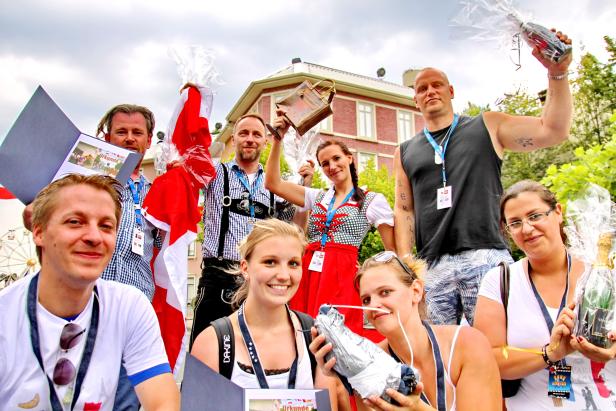 Eine Gruppe von Menschen feiert mit Urkunden, einer Schweizer Flagge und Getränken vor einem Gebäude.