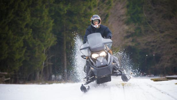 Eine Person fährt mit einem Schneemobil durch eine verschneite Landschaft.