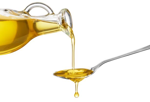 Öl wird aus einer Glasflasche in einen Löffel gegossen.
