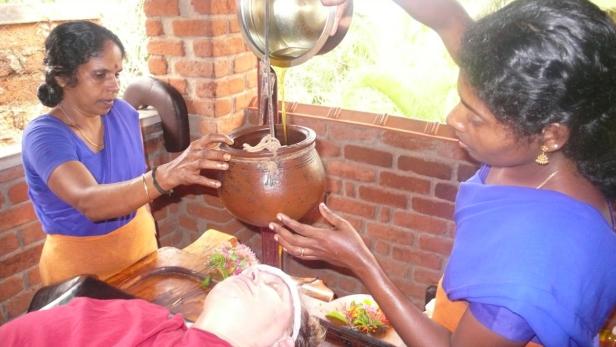 Zwei Frauen führen eine ayurvedische Ölbehandlung an einem Patienten durch.