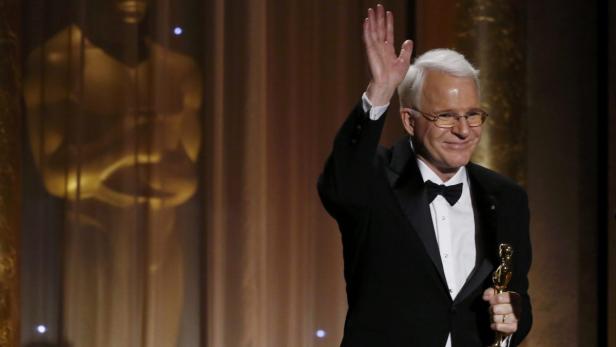 Steve Martin hält eine Oscar-Statue und winkt.
