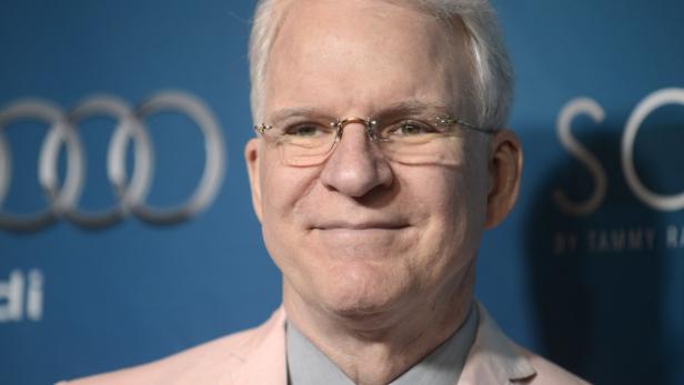Porträt von Steve Martin mit Brille vor einem blauen Hintergrund.