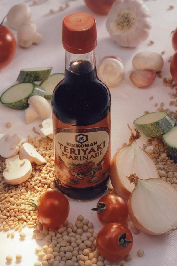 Eine Flasche Kikkoman Teriyaki Marinade umgeben von Gemüse und Sojabohnen.