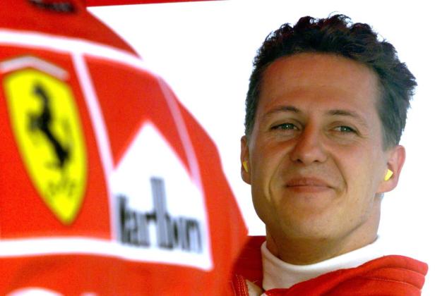 Michael Schumacher mit Ohrstöpseln neben einem Ferrari-Rennwagen.