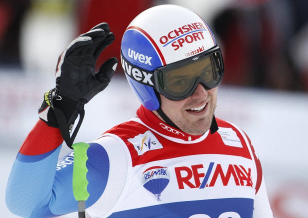Ein Skirennläufer mit Helm und Skibrille winkt in die Kamera.