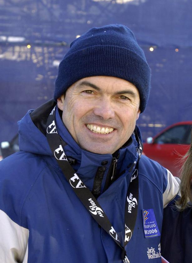 Ein lächelnder Mann mit Mütze und Jacke vor einem unscharfen Hintergrund.