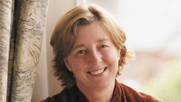 Eine lächelnde Frau mit blonden Haaren vor einem Fenster.