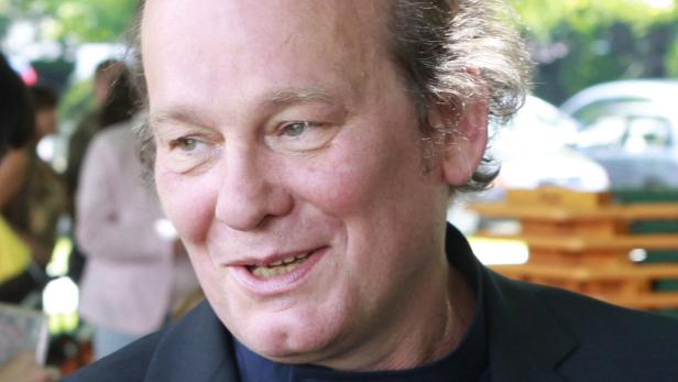 Ein Mann mit dunklem Jackett lächelt in die Kamera.