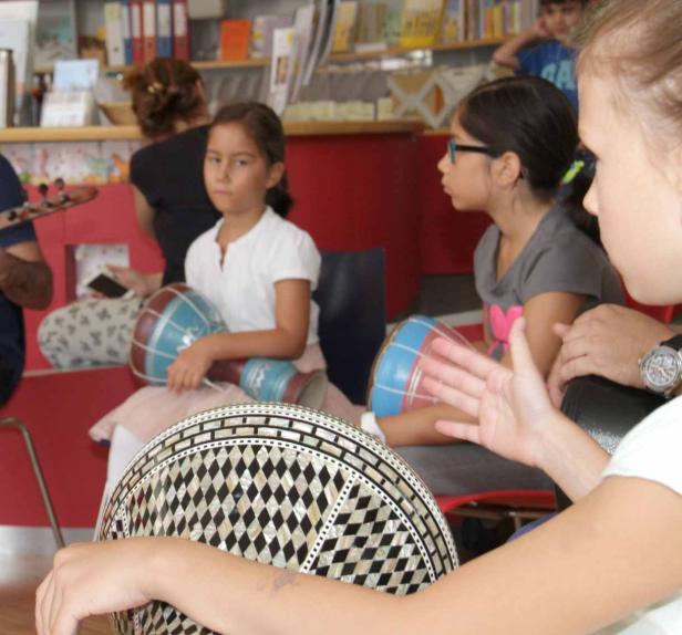 Kinder sitzen im Kreis und spielen auf kleinen Trommeln.