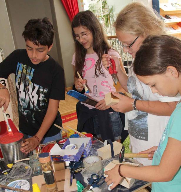 Eine Gruppe Kinder bastelt mit Farbe, Holz und Werkzeugen an einem Tisch.