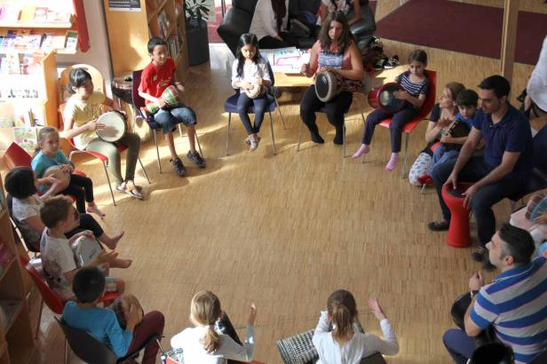 Eine Gruppe von Kindern und Erwachsenen sitzt im Kreis und spielt auf Trommeln.