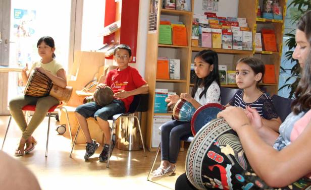 Eine Gruppe Kinder sitzt auf Stühlen und spielt auf verschiedenen Trommeln.