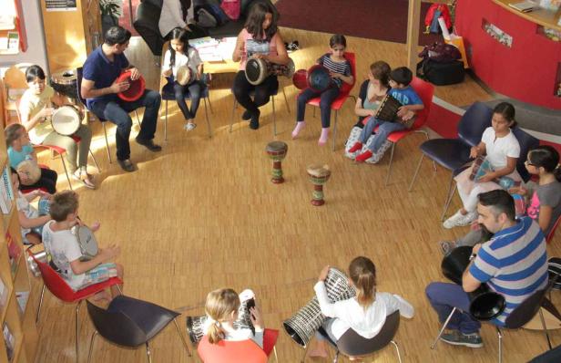Eine Gruppe von Kindern und Erwachsenen sitzt im Kreis und spielt auf Trommeln.