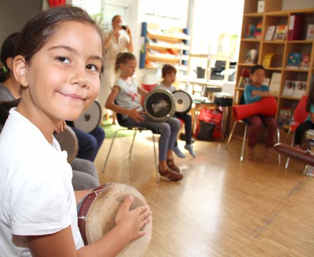 Eine Gruppe Kinder sitzt im Musikunterricht und spielt auf Trommeln.