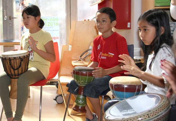 Drei Kinder sitzen und spielen auf verschiedenen Trommeln.